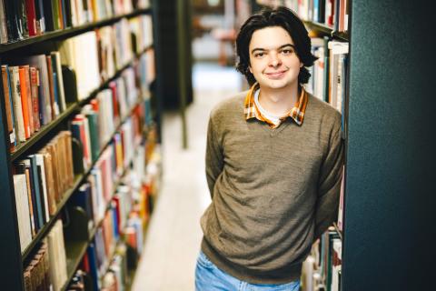 Jack Ciavolella stands in the stacks, leans against a bookshelf, and smiles at the camera.